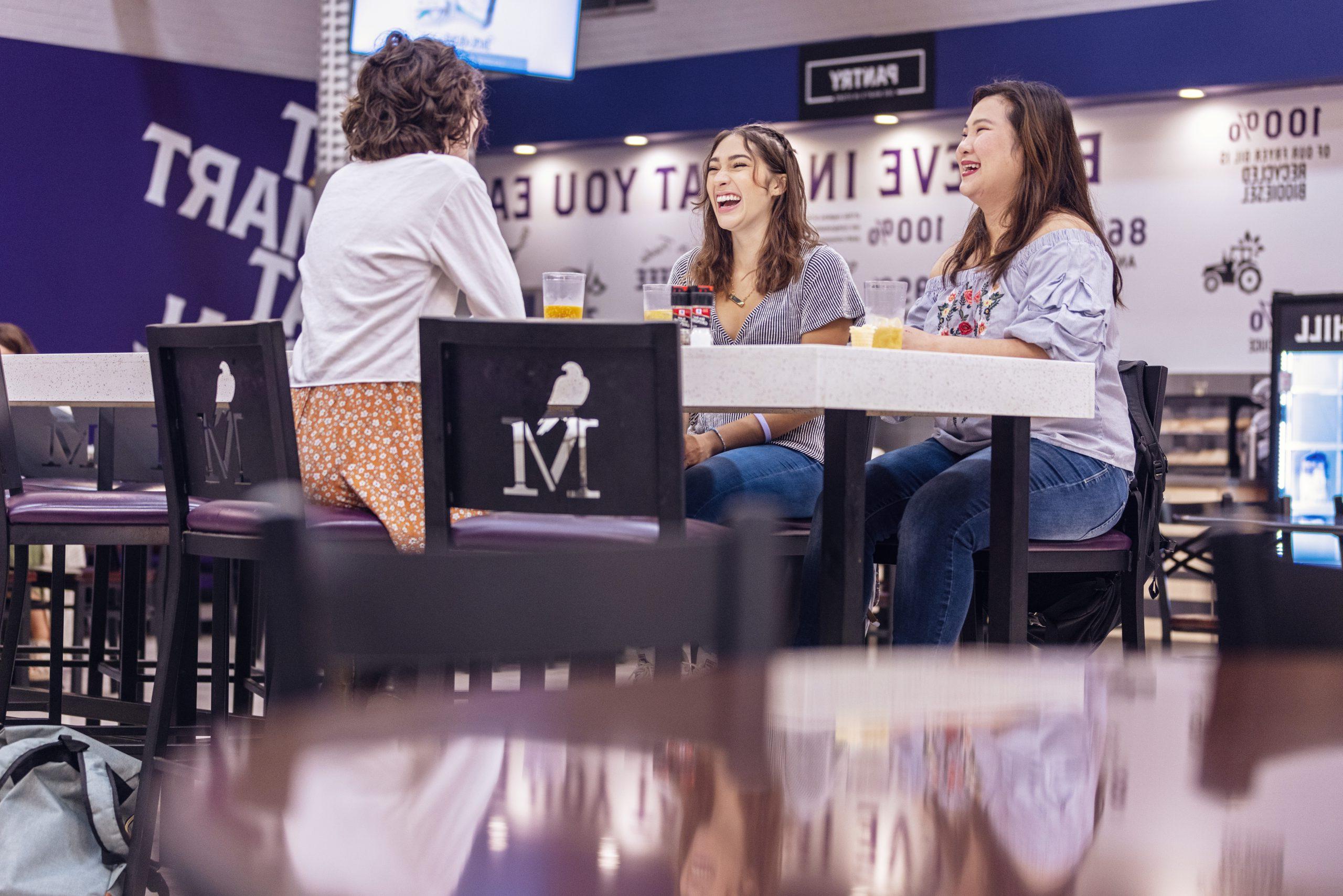 University of Montevallo students smile as they chat while sitting at a table in Anna Irvin Hall.